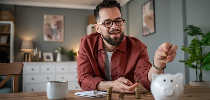 Young,Man,Smiling,As,He,Drops,Coins,Into,A,White