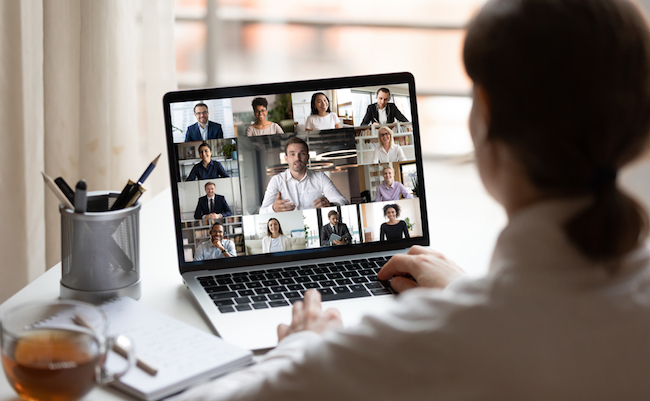 View over businesslady shoulder seated at workplace desk look at computer screen where collage of many diverse people involved at video conference negotiations activity, modern app tech usage concept