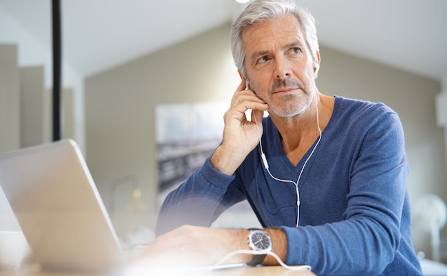 Senior man working on laptop and using earphones for virtual meeting