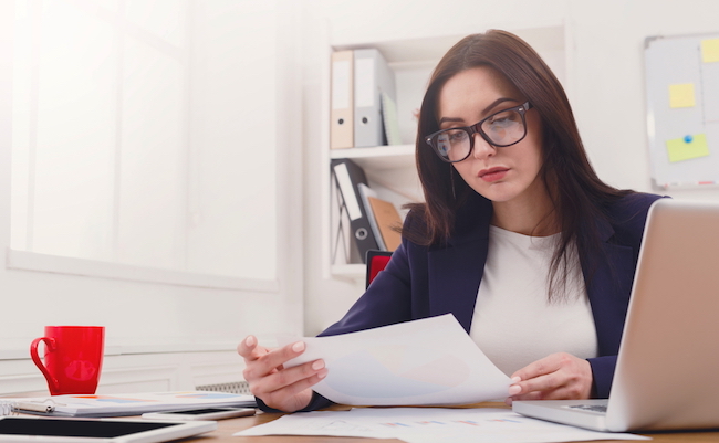 Paperwork. Serious business woman in formal wear sitting at wooden desk in modern office and reading report document, copy space