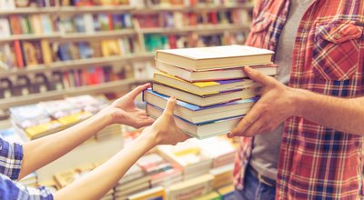 Cropped image of young man and woman holding a pile of books while standing in the book shop