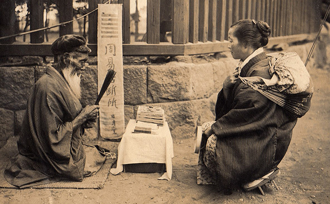 1280px-Fortune_Teller_on_the_street_of_Japan_(1914_by_Elstner_Hilton)
