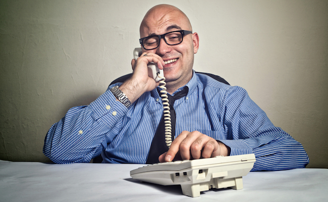 Smiling,Businessman,At,Office,Desk,With,Telephone.,Wheeler,Dealer,Or