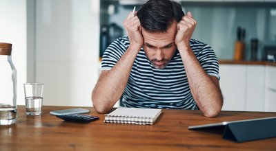 Sad man looking at notebook with home budget and stressing over money