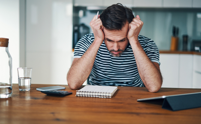 Sad,Man,Looking,At,Notebook,With,Home,Budget,And,Stressing