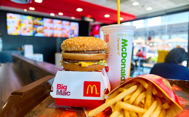 BANGKOK, THAILAND- JULY 26, 2020 : Tasty Big Mac hamburger, french fries, and cup of drink served in retail background of McDonald's restaurant. A popular American fast food chain. Selective focus.