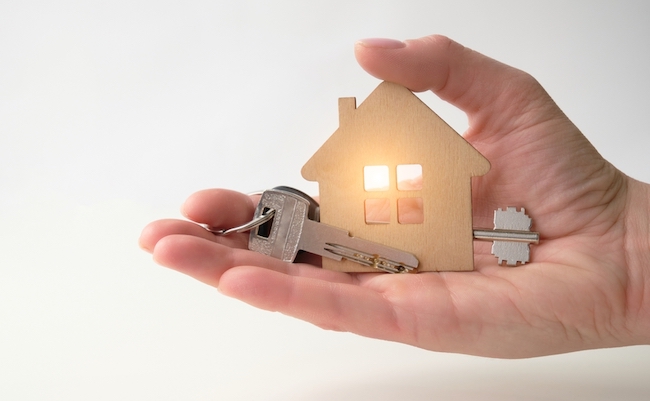 A,Woman’s,Hand,Holds,A,Model,Of,A,Wooden,House