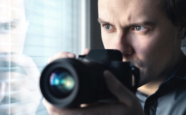 Private detective, undercover cop, investigator, spy or paparazzi with camera taking photos. Agent or police spying, investigating or following people. Espionage or surveillance concept. Man hiding.