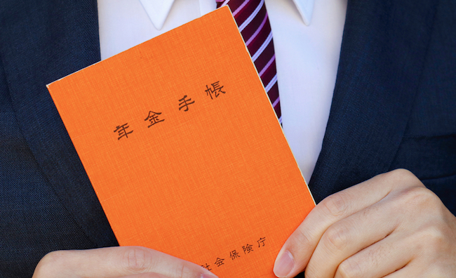 A man in a suit. An orange notebook with Japanese writing. Translation: Pension Handbook, Social Security Administration.