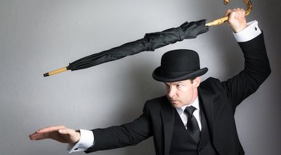 Portrait of British Spy in Dark Suit and Bowler Hat Holding Umbrella Like a Sword. Concept of Vintage Film Noir Action Hero in Fighting Stance.