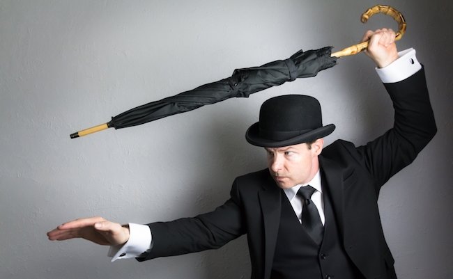 Portrait of British Spy in Dark Suit and Bowler Hat Holding Umbrella Like a Sword. Concept of Vintage Film Noir Action Hero in Fighting Stance.