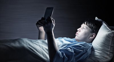 Young teenager guy in bed using tablet pc