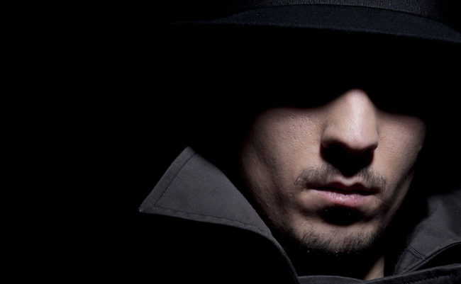 young criminal in shadow, isolated on a black background