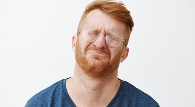 Close-up shot of cute and funny adult with red hair and beard, crying and being gloomy, closing eyes, frowning, tilting head back while pursing lips, feeling regret or upset over gray background