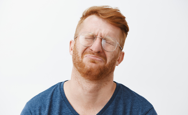 Close-up shot of cute and funny adult with red hair and beard, crying and being gloomy, closing eyes, frowning, tilting head back while pursing lips, feeling regret or upset over gray background