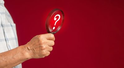 Question mark concept. Close-up of hand a senior man holding a magnifying glass looking at a question mark symbol while standing over a red background