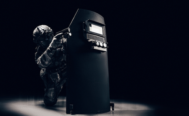 Portrait of a special forces unit fighter. He hides behind a bulletproof shield. Black background. The concept of the fight against terrorism. Mixed media