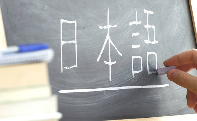 Hand writing some the word "Japanese" in Kana syllabary on a blackboard in a Japanese class. Some books and school materials.