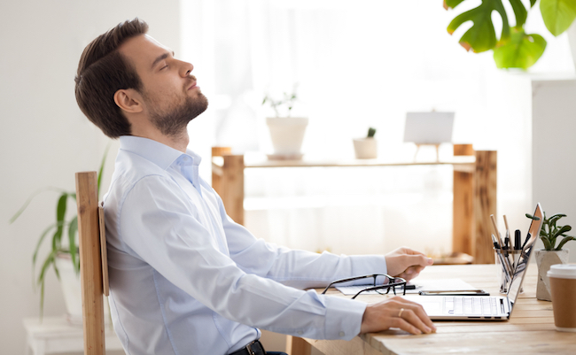 Satisfied calm businessman taking break to relax finished work sitting at desk enjoying stress free job breathing fresh air, happy executive manager resting at workplace dreaming in quiet office