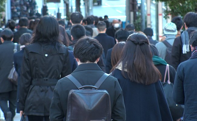 Back shot of unidentified crowd of people walking down the street in busy rush hour. Many commuters going to work. Japanese business man and woman, job and lifestyle concept.