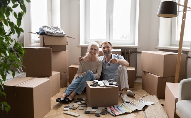 Happy spouses sit on floor near boxes with belongings smile showing keys from new house. Redecoration or repair works of dwelling, homeowners portrait, bank loan for older citizen, remodelling concept