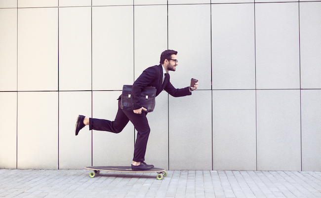Toned image of businessman in black business suit on longboard walking with cup of coffee in his hand. Freelance man hurrying to his office.