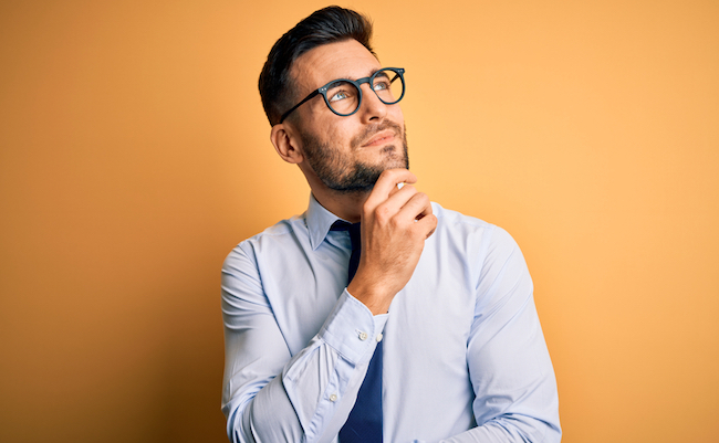 Young,Handsome,Businessman,Wearing,Tie,And,Glasses,Standing,Over,Yellow