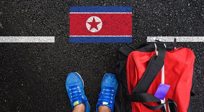 a man with a shoes and travel bag is standing on asphalt next to flag of North Korea and border