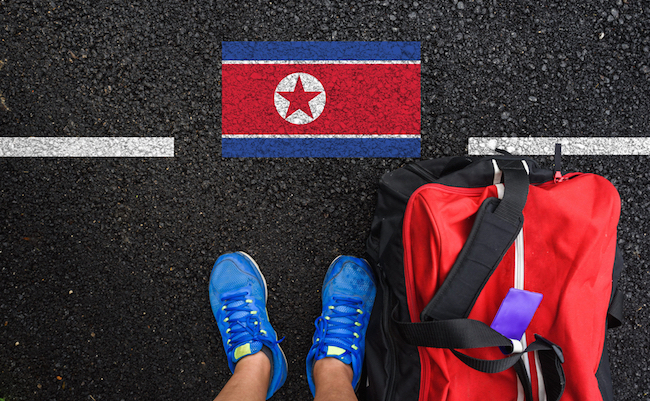 a man with a shoes and travel bag is standing on asphalt next to flag of North Korea and border