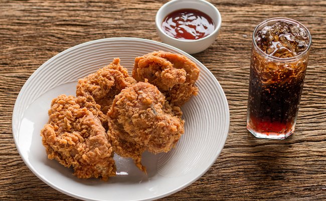 fried chickens breast (on white dish) with cola and ketchup on wood board.
