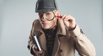 Male detective looking through magnifying glass on grey background
