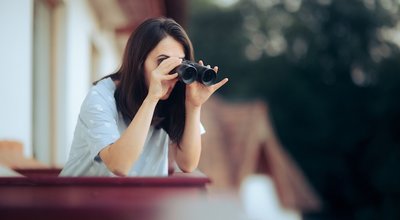 Curious Woman Holding a Pair of Binocular Spying on her Neighbors. Funny young person snooping and peeping from her balcony