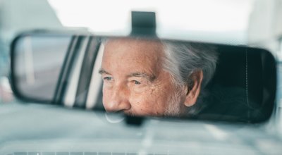 Portrait of one old pensioner man driving and enjoying his new car. Rear view mirror.