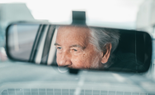 Portrait of one old pensioner man driving and enjoying his new car. Rear view mirror.