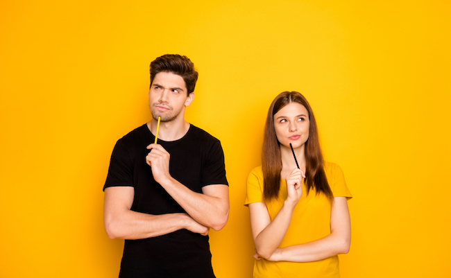 Photo of serious confident couple of two people interested in thinking over standing under empty space holding pens wearing black t-shirt isolated over vivid yellow color background