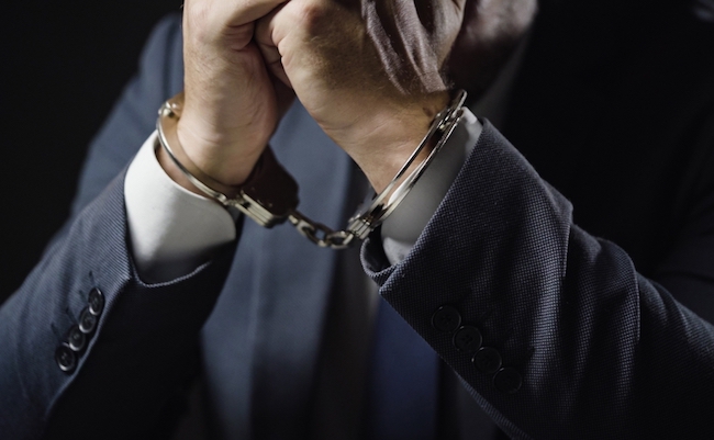 Businessman in handcuffs arrested for financial fraud, sitting in interrogation room