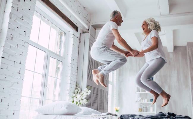 Love lives forever! Senior couple at home. Handsome old man and attractive old woman are enjoying spending time together. Having fun and jumping in bed.