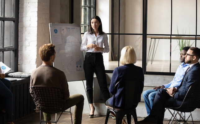 Confident lady business trainer coach leader give flip chart presentation consulting clients teaching employees training team people speaking explaining strategy at marketing workshop concept