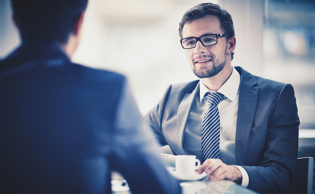 Image of young businessman with cup of coffee communicating with his colleague