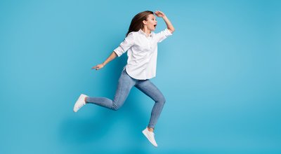 Full length photo lady jump high running look far away interested wear white shirt jeans shoes isolated blue color background