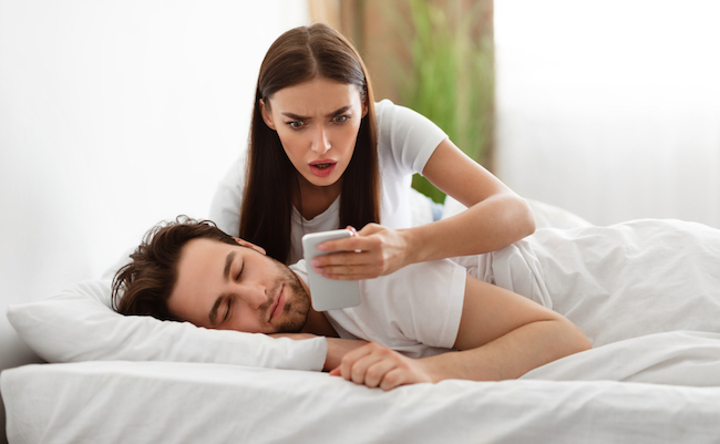 Infidelity. Shocked Wife Reading Message From Lover On Phone While Cheating Husband Sleeping In Bedroom At Home. Jealous Woman Checking Boyfriend's Cellphone Chats. Affair, Relationship Issues