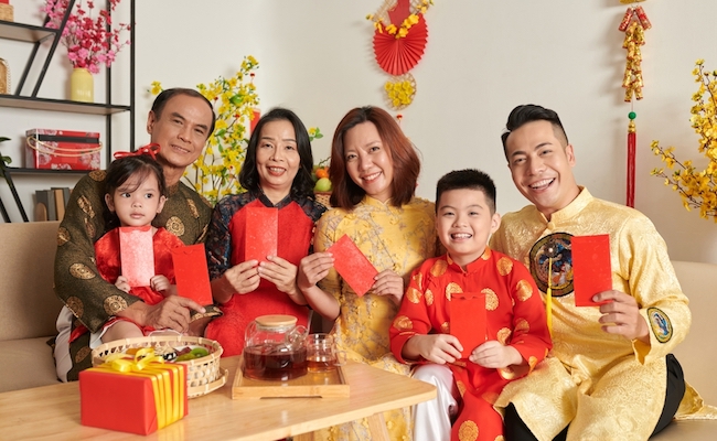 Smiling family members in ao dai dresses holding red lucky money envelopes