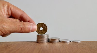 Hand put five Japanese coin on top roll of money on wood table in white background