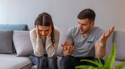 Unhappy couple having an argument in living room at home. Woman sitting at home. Sad pensive young girl thinking of relationships problems sitting on sofa with offended boyfriend,conflicts in marriage