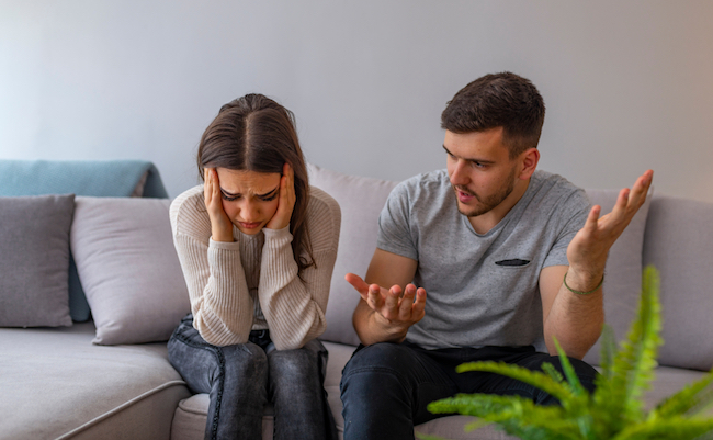 Unhappy couple having an argument in living room at home. Woman sitting at home. Sad pensive young girl thinking of relationships problems sitting on sofa with offended boyfriend,conflicts in marriage