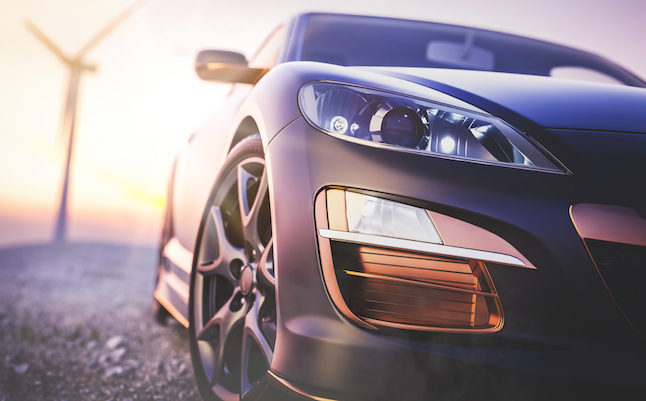 The image in front of the sports car scene behind as the sun going down with wind turbines in the back.