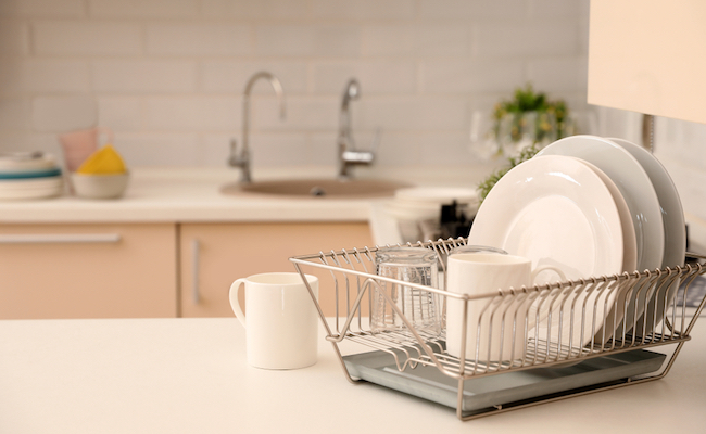 Dish drainer with clean dinnerware on table in kitchen. Space for text