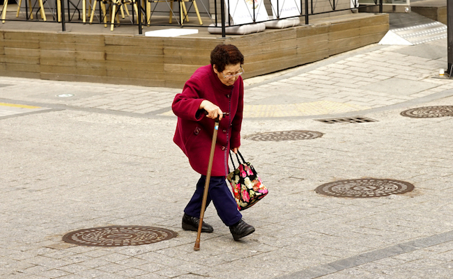 Seoul, Republic of Korea - March 2019: An eighty year old woman with a stick crosses the road.