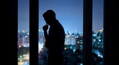worried asian young businessman is standing near windows while working overtime in office at night