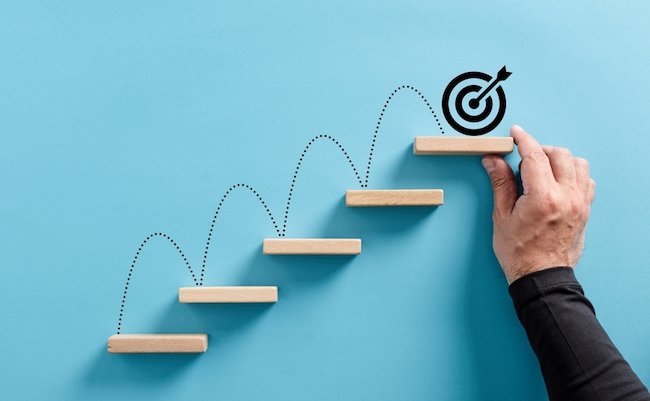 Male hand arranges a wooden block staircase with target icon. Achieving goals and objectives or goal setting concept.